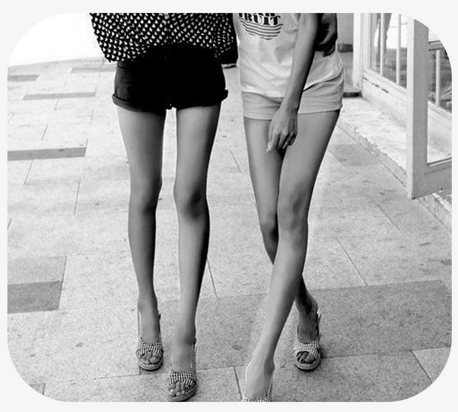 Two females friends walking together, one with her legs crossed over