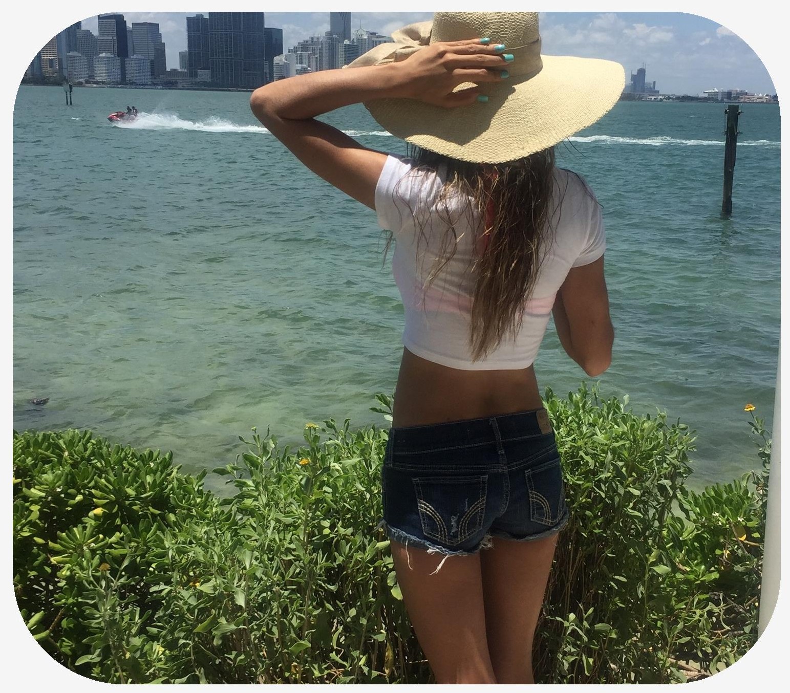 Rear view of a woman in a bikini wearing a hat looking over the water