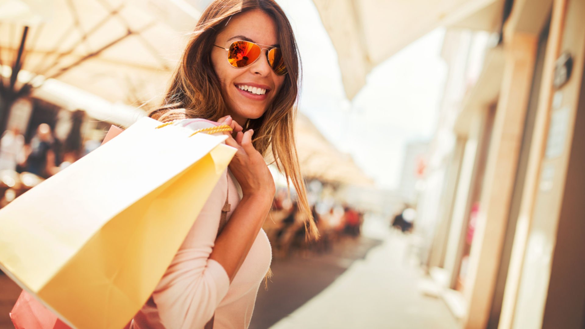 Woman wearing sunglasses, walking outside while holding a shopping bag