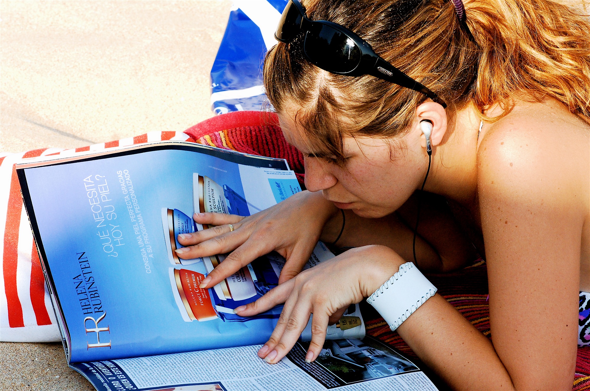Girl on the beach, on top of a towel, Reading a magazine