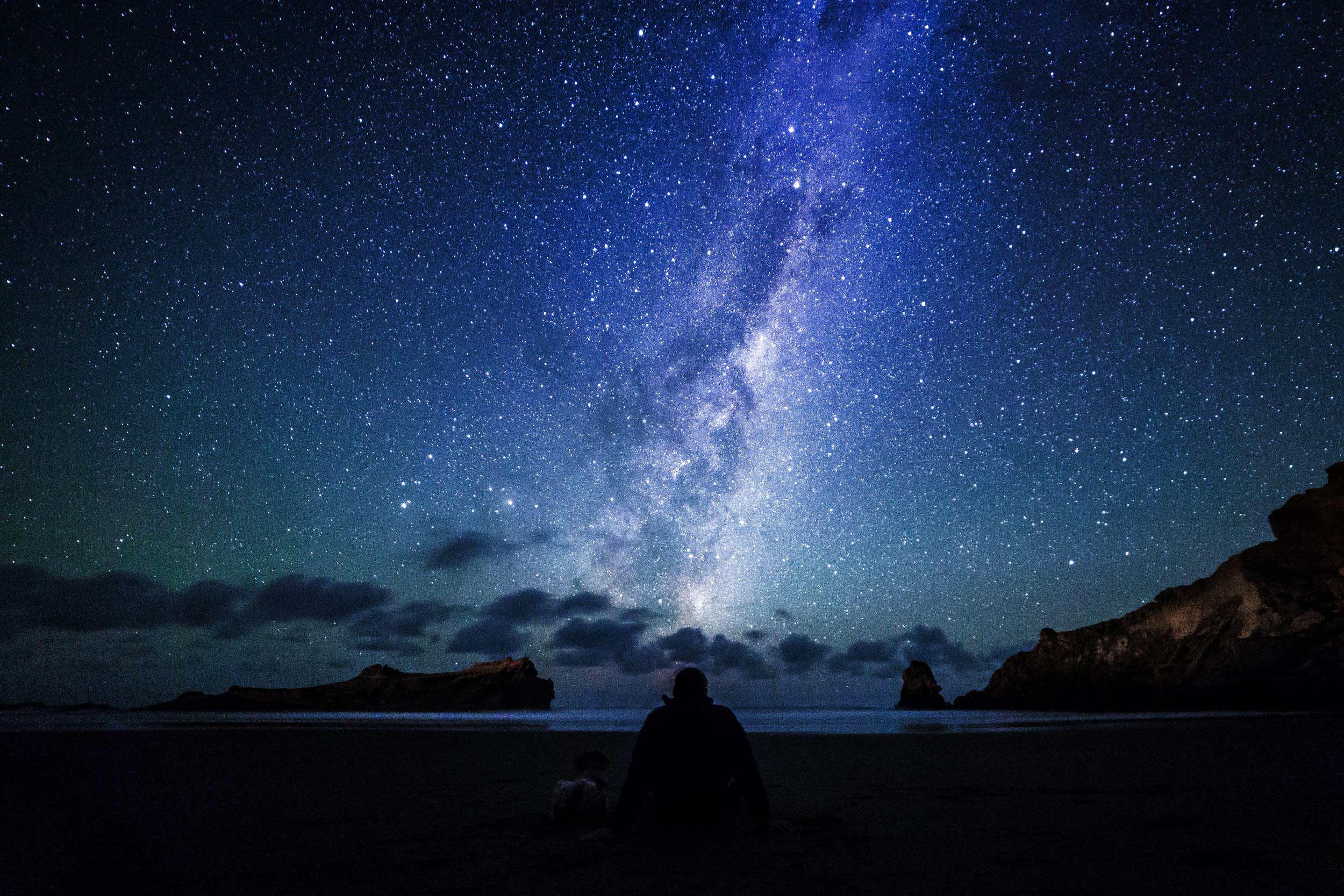 Person sitting on a beach in the dark, watching the stars