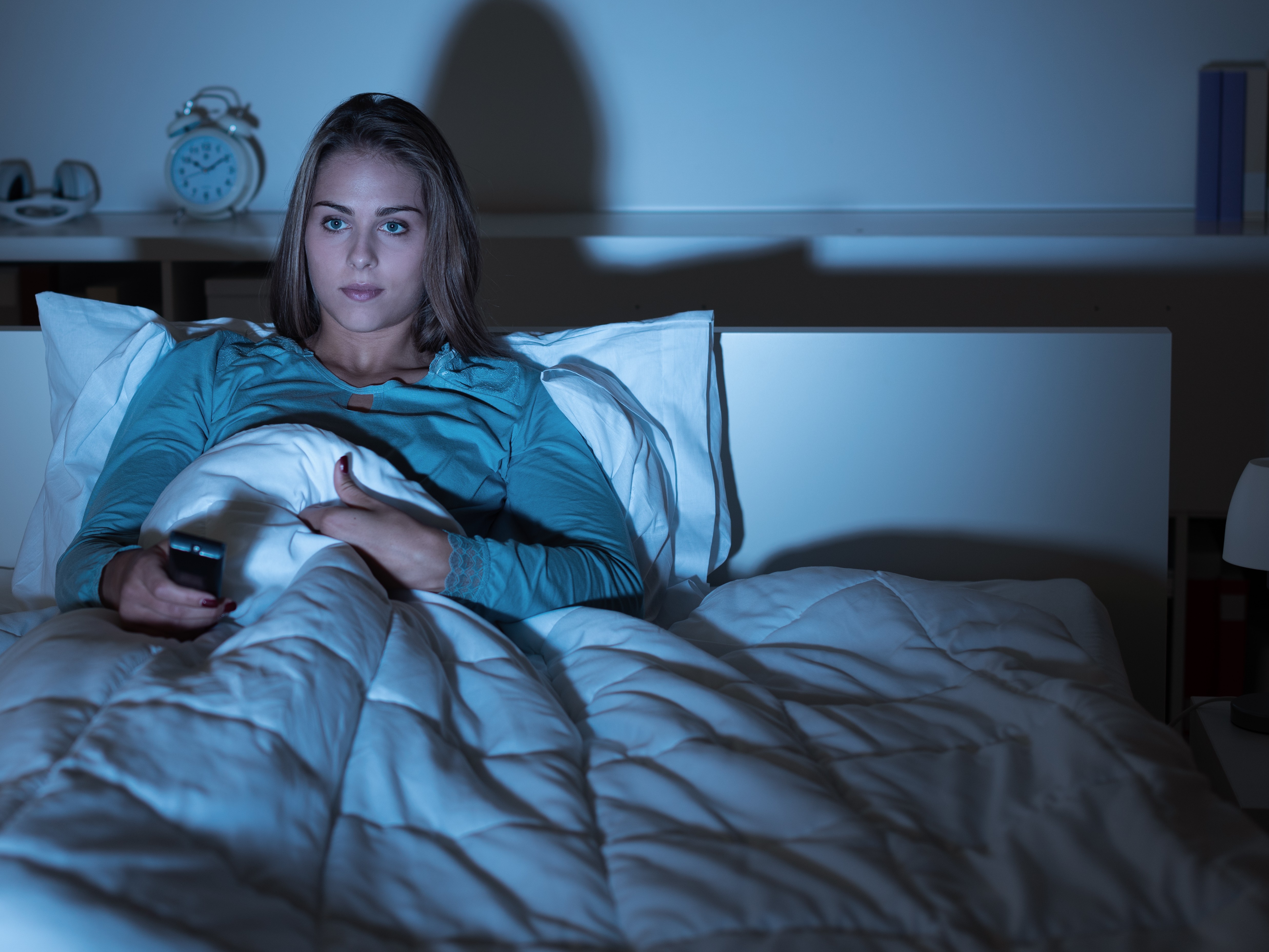 Woman under the covers, on a bed, watching a movie in the dark
