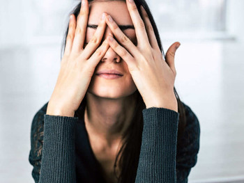 Woman sitting down with hands covering her face.